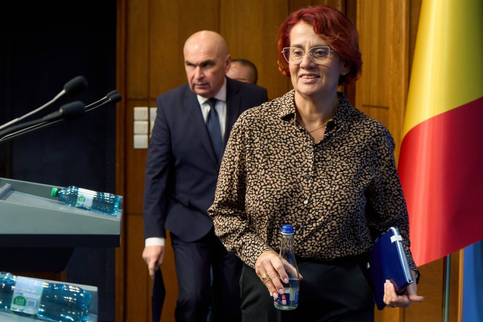 Ioana Ene Dogioiu, purtătoarea de cuvânt a Guvernului, avându-l pe Ilie Bolojan în spate